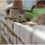 Worker laying brick onto new construction wall